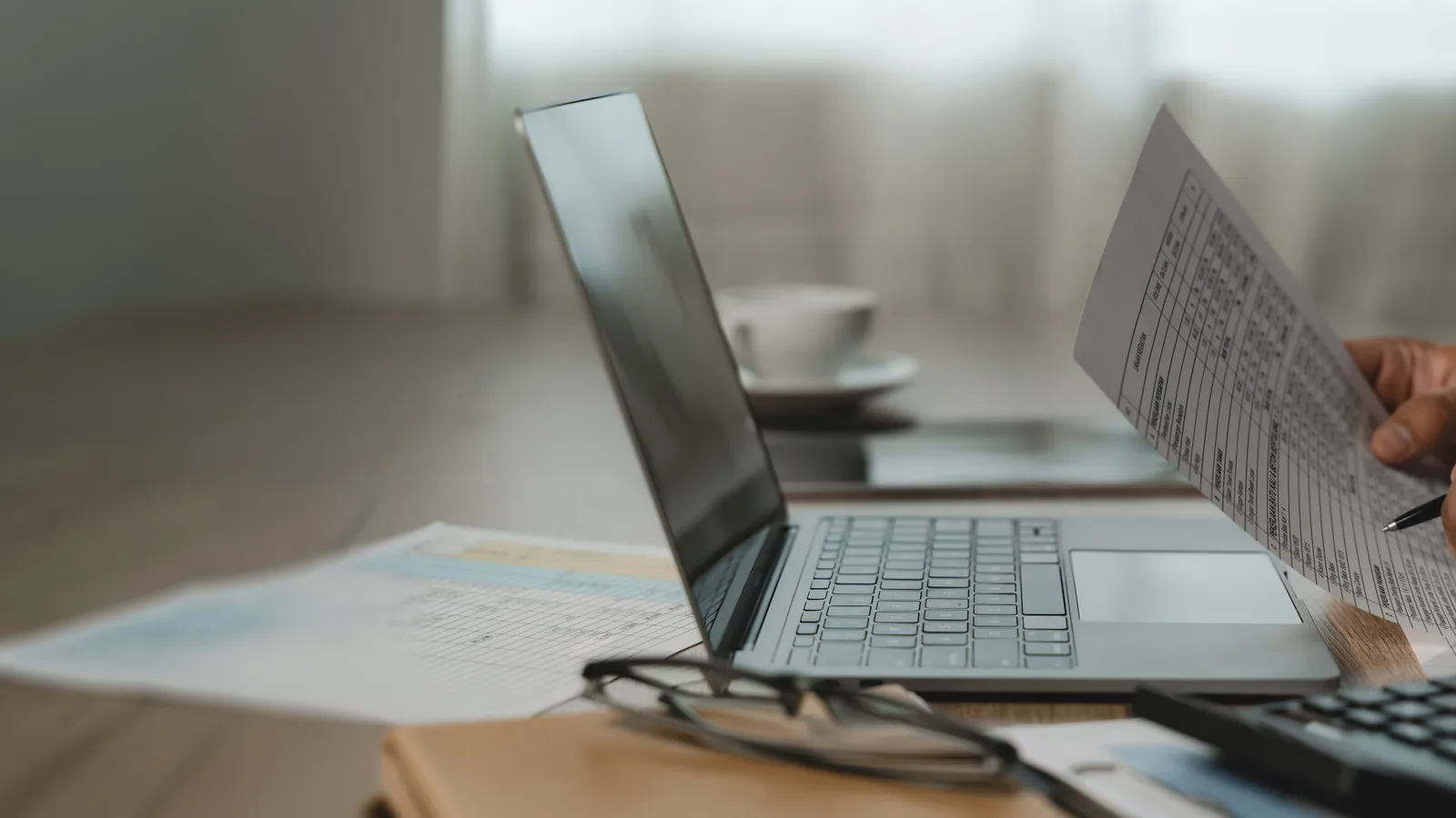 Hands reviewing a financial document beside a laptop and a calculator.