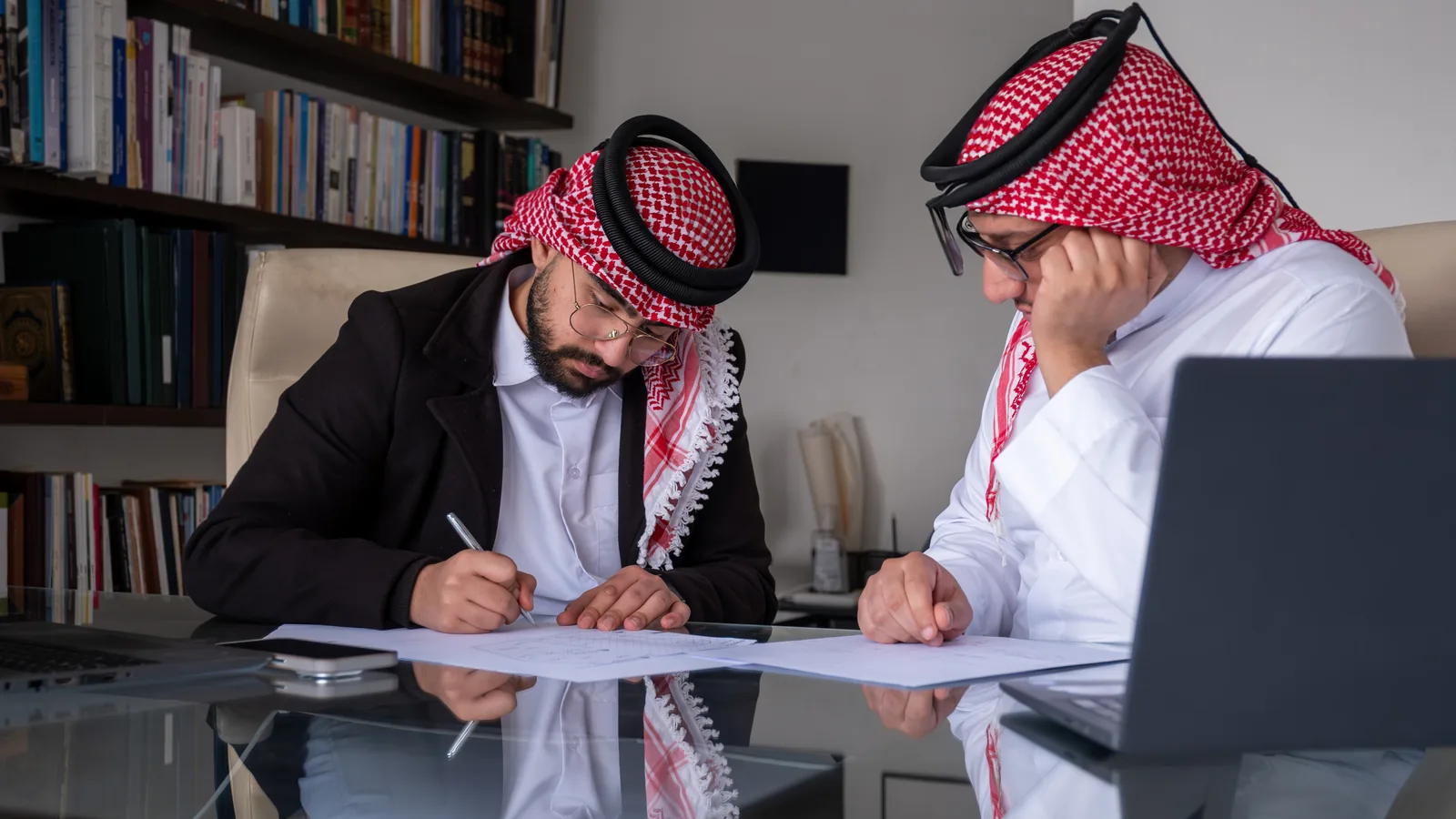 Two founders in ghutra working through company papers together at a desk.